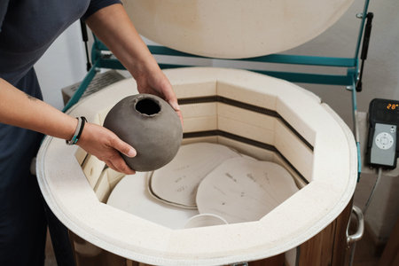 close-up of hands putting vase into the kiln, oven for roasting of unbaked clay handmade products,...