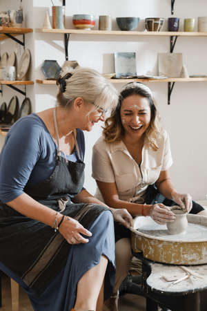 Teacher and student at pottery workshop learning to make bowls from clay. Happy woman doing handmade dishes. Lesson for adults at ceramics studioの写真素材