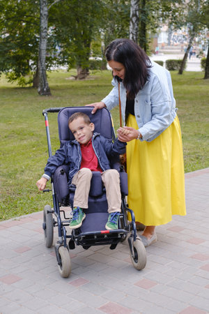 Family with cerebral palsy child on special wheelchair walking outdoors. Integration and accessibility of disabled people, inclusion. Brother with physical disorder Mother taking care of handicap kidの写真素材