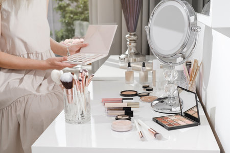 Make-up table, decorative cosmetics for professional and home makeup. Close-up view of brushes, eyeshadow palates in white sunny salon. Beauty Artists hands choosing color of base. Copy spaceの写真素材