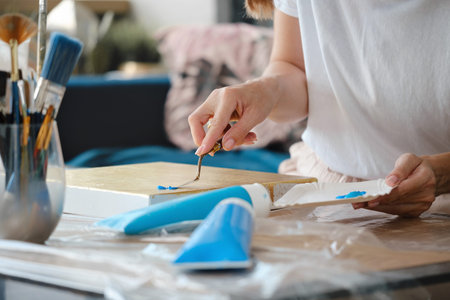 Painter hand with spatula, close-up art work with acrylic paints on canvas. Artist working in...