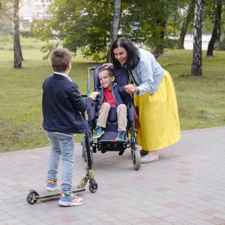 Family with child that has cerebral palsy, wheelchair user walking outdoors. Integration and accessibility of people with limited abilities, inclusion. Brother having illnessの写真素材