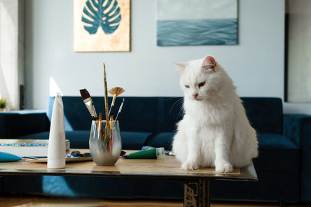 White cat sitting on the table near paintbrushes over the wall. Copy space for artistの写真素材
