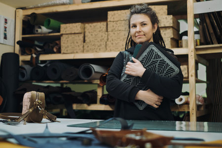 Tailoring eco leather laptop cases. Woman designer posing with eco leather textile product at her workshop. Handmade and craft production conceptの写真素材