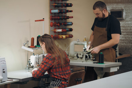 Workers sewing on professional sewing machine at workshop. Tailor making accessories from eco leather. Craft production concept. People working in leather manufacture. Small businessの写真素材