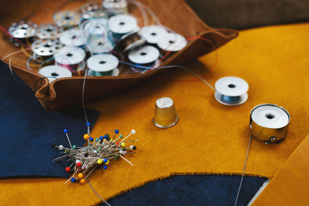 Tailor workplace accessories. Close up view of the eco leather and tailoring equipment laying on the table. Set of pins, bobbin for a sewing machine, spool of thread, top viewの写真素材