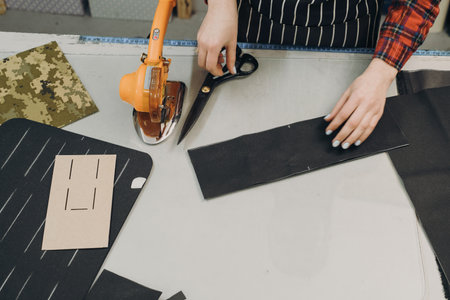 Seamstress at work. Dressmaker cutting fabric. Woman standing at table with cut textile and working on a design. Top view, closeup with copy space. Disc cutting knifeの写真素材