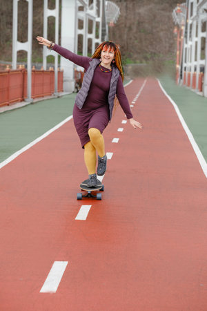 Funny free hipster Woman with dreadlocks on longboard on the road riding in the city at her 30s. female with bright colorful hair enjoy outdoor active lifestyle, play extreme sportの写真素材