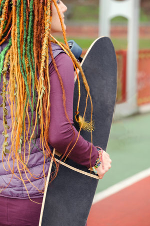 Funny free hipster Woman with dreadlocks holding longboard on the road riding in the city at her...