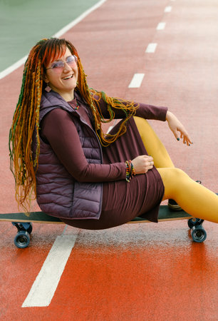Funny free hipster Woman with dreadlocks sitting on longboard on the road riding in the city at her 30s. female with bright colorful hair enjoy outdoor active lifestyle, play extreme sportの写真素材