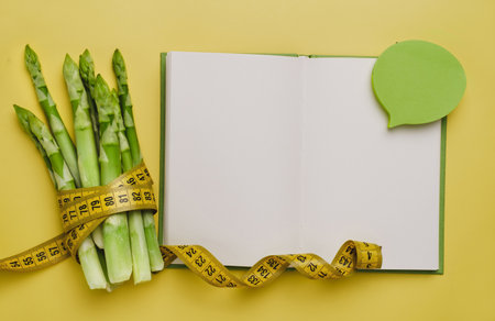 Asparagus and measuring tape isolated yellow. Diet and balanced nutrition food for weight loss concept. Copy space in notebook for recipeの写真素材