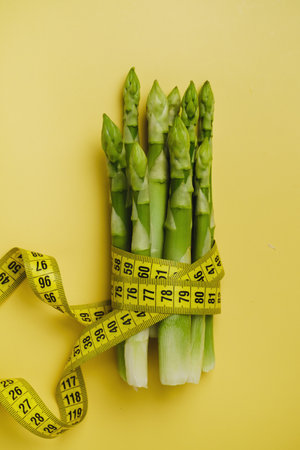Asparagus and measuring tape isolated yellow. Diet and balanced nutrition food for weight loss conceptの写真素材