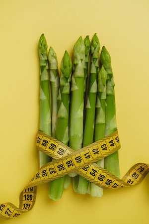 Asparagus and measuring tape isolated yellow. Diet and balanced nutrition food for weight loss conceptの写真素材
