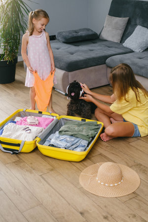 Children packing suitcase for travel and play with a dog. Sisters having fun with pet while getting ready for a trip. Dog in sunglasses and sunhat. going on vacationの写真素材
