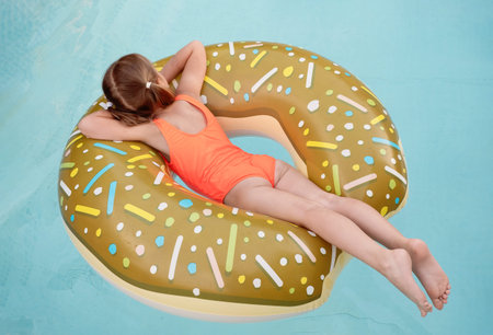Happy preschool girl in outdoor swimming pool on inflatable ring. Child enjoying summer time...