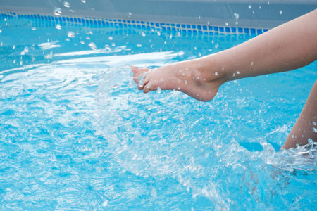 Kids legs splashing in water near swimming pool outdoors. Summertime activities for children. Copy...