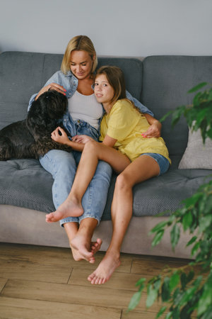 Young loving mother hugging her teenage daughter, mom demonstrating unconditional love for child, mommy cuddling supporting teen girl while spending time together at home with dogMother-daughter bondの写真素材