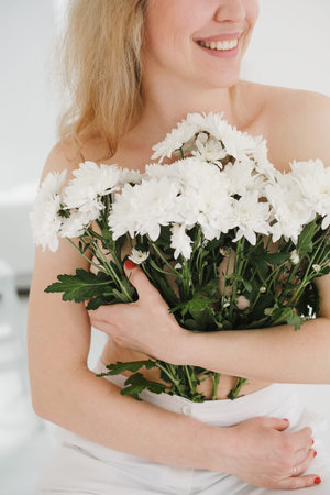 Hugging white flowers. Close up of unrecognizable smiley woman covered with bouquet on whiteの写真素材