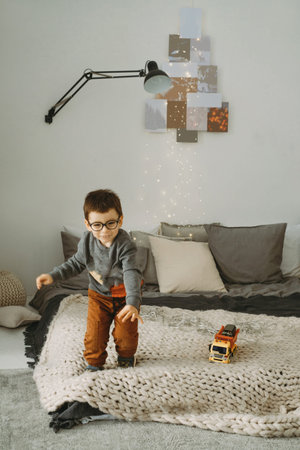 Toddler child jumping on the bed on Christmas morning. Happy boy in eyeglasses jumping at homeの写真素材