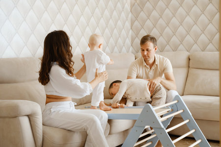 Family with two kids on the couch having fun. Mather, father baby and toddler sons are happy in the morning in Livingroom. Children playing on Toddler Indoor Gym Playset for children, ladder Climbingの写真素材