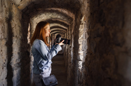 Woman taking pictures in old tunnel, looking in window and walking through. Female visiting castle. Traveling in ancient buildingの写真素材