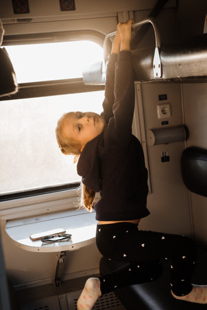 Happy child riding in train on sunset, bright sunlight, atmospheric travel by railway with kids. Young passenger playing on the couch of slipping wagon. Long family tripの写真素材