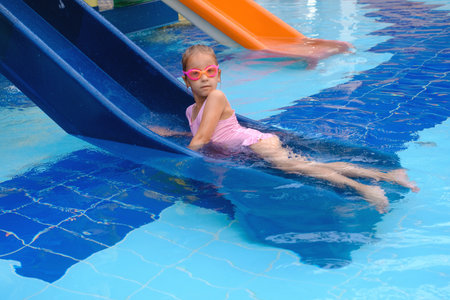 Child sliding into the water in aqua park. Kid having fun and entertaining in indoor swimming pool. Toddler girl laying in the water.の写真素材