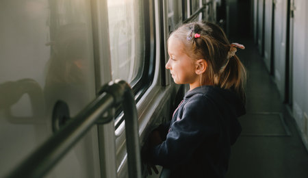 Toddler child looking through train window on sunset, bright sunlight, atmospheric travel by railway with kids. Girl happy exploring the way in evening. Exciting family tripの写真素材