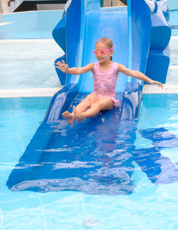 Child sliding into the water in aqua park. Kid having fun and entertaining in indoor swimming pool....