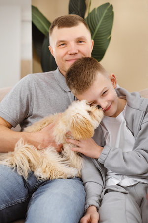 Man and boy sitting on couch with a dog, relaxing indoors with family.の写真素材