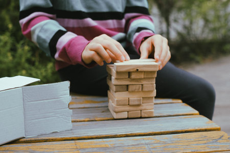 Person stacking wooden blocks, building tower while seated at a table outdoors, concentrating on balancing the pieces. Closeupの写真素材