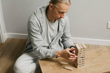 Person is carefully stacking blocks in wooden tower game in the room at home. Digital detox and...