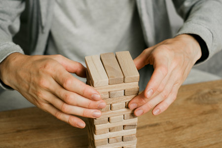 person stacks wooden blocks to construct tower on table in a room, Man playing table game for concentration at home. Digital detoxの写真素材