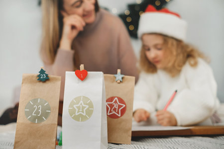Mother with toddler girl writing Christmas letter and doing advent calendar tasks in bedroom. Festive activities for children at home. Happy dreaming girl creating craftの写真素材