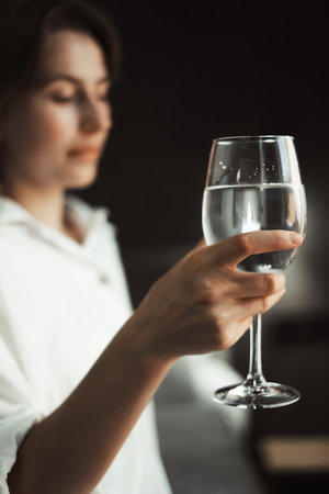 Woman holds glass of water, reflecting her solitude. She appears lost in thought, dehydrated, encapsulating the essence of lonely travel moments.の写真素材