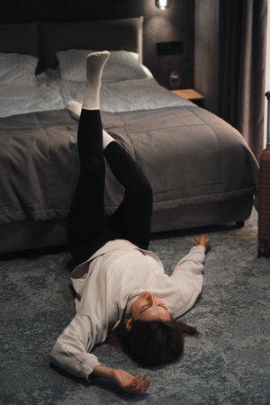 Emotionally exhausted woman relaxing in a hotel room after solo travel. Female with suitcase having frustration or abuse. Dark hotel room with curtains, quit and solitudeの写真素材