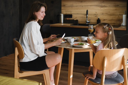 Mother and daughter having meal together in a stylish, contemporary home. Family eating delicious breakfast on the kitchenの写真素材