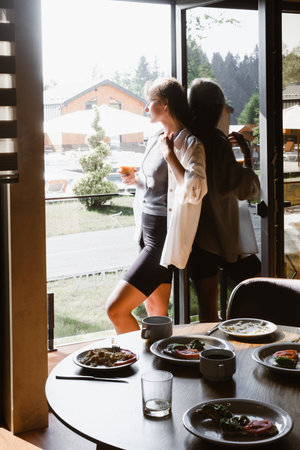Relaxing in a modern hotel dining area with scenic view. Woman enjoys drink while looking out of large window in a contemporary hotel. Table is set with delicious meal, cozy atmosphereの写真素材