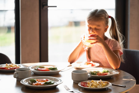 young girl smiles drinking glass of juice and enjoys whole grain toast topped with fresh tomatoes and avocado.の写真素材