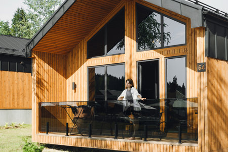 Woman enjoying rest in a modern hotel cabin. Woman standing on the balcony of wooden house. Vacation and travel in summer outdoor. Cozy house for recreationの写真素材