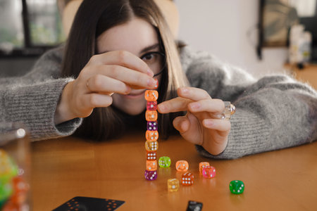 Woman building colorful stack of dice during tabletop game in bright living room. Happy smiley female enjoy playing game at homeの写真素材