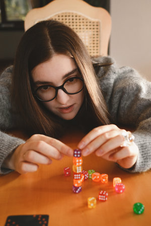 Woman building colorful stack of dice during tabletop game in bright living room. Happy smiley female enjoy playing game at homeの写真素材
