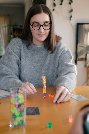 Woman building colorful stack of dice during tabletop game in bright living room. Happy smiley female enjoy playing game at homeの写真素材