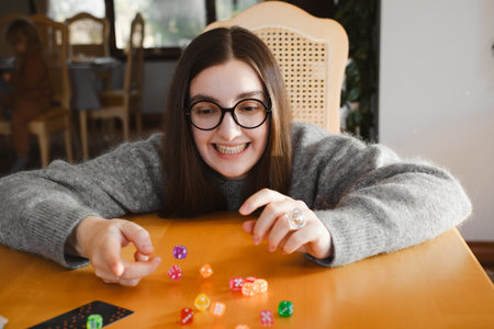 Woman building colorful stack of dice during tabletop game in bright living room. Happy smiley female enjoy playing game at homeの写真素材