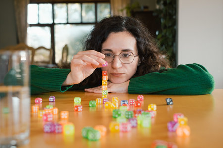 Woman player at her 40s stacking colorful dice during table game night. Female enjoys activity and fun free time entertainmentの写真素材