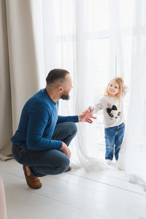 Father lifts his daughter joyfully in bright and airy living room. Large windows, creating a warm and loving atmosphere. Active game and parenting. Fathers dayの写真素材
