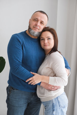 man and woman stand together, embracing each other in a warm home environment. Couple shares moment of affection, representing love and family bonds in their living space. People at their 50s and 40sの写真素材