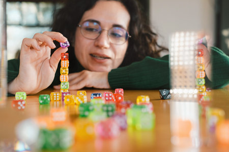 Woman player at her 40s stacking colorful dice during table game night. Female enjoys activity and fun free time entertainmentの写真素材