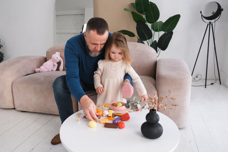 Father at home with child plays toy kitchen at home. Toddler daughters and dad spend time togetherの写真素材