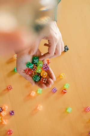 Dice in woman hands. Table games concept. Closeup of colorful playing accessories over yellow table. Copy space. Gather green dice in female hands, preparing for an exciting leisure timeの写真素材